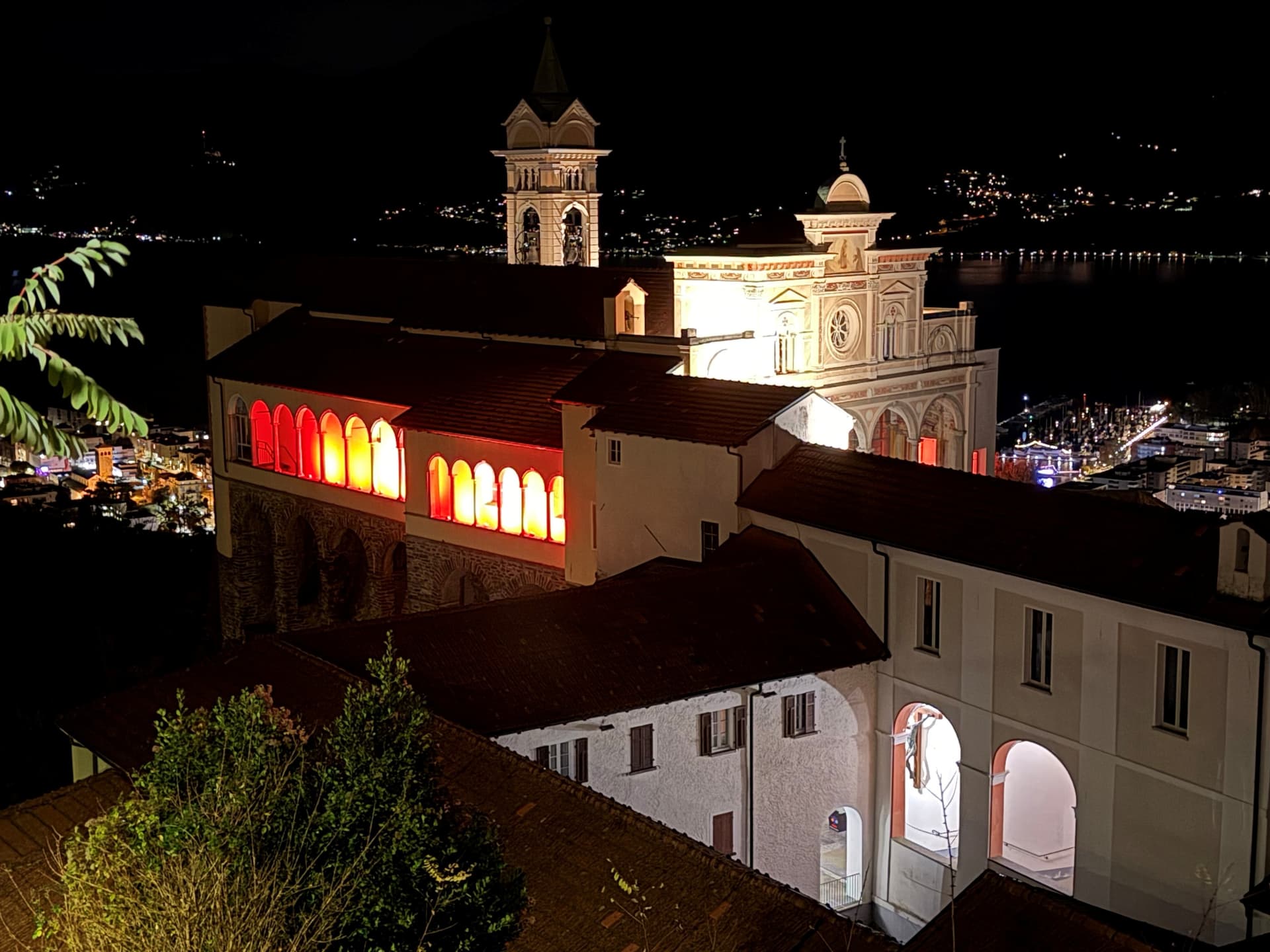 REDWEEK 2025 Orselina santuario della Madonna del Sasso illuminato di rosso vista da Orselina su Locarno e Gambarogno 2